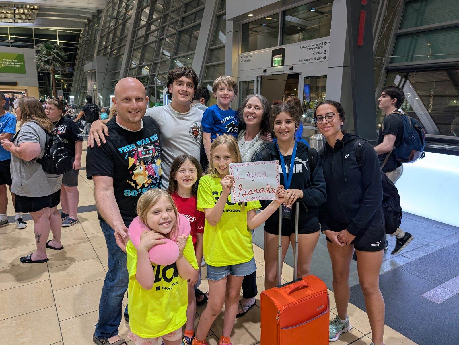 Familia anfitriona recibiendo a una estudiante con un cartel de bienvenida en el aeropuerto